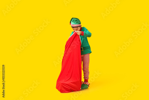 Cute little elf with bag of gifts on yellow background