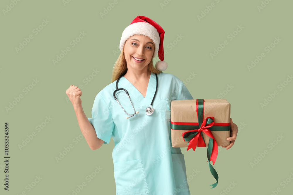 Mature female doctor in Santa hat with Christmas gift box on green background Mature female doctor in Santa hat with Christmas gift box on green background