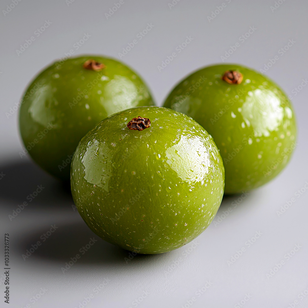 Obraz premium Three shiny green fruits arranged closely on a gray surface.