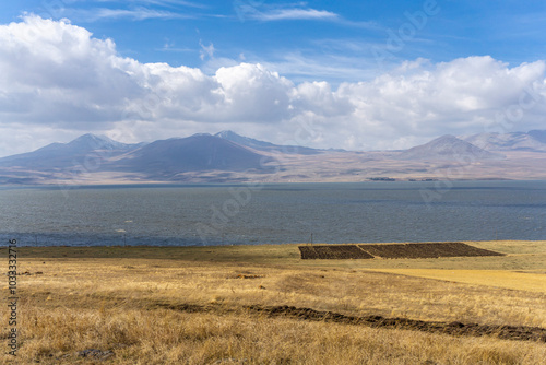 A ploughed field among dry yellow grass on the edge of Lake Paravani. Mountains, hills and a bright sky with clouds in the background photo