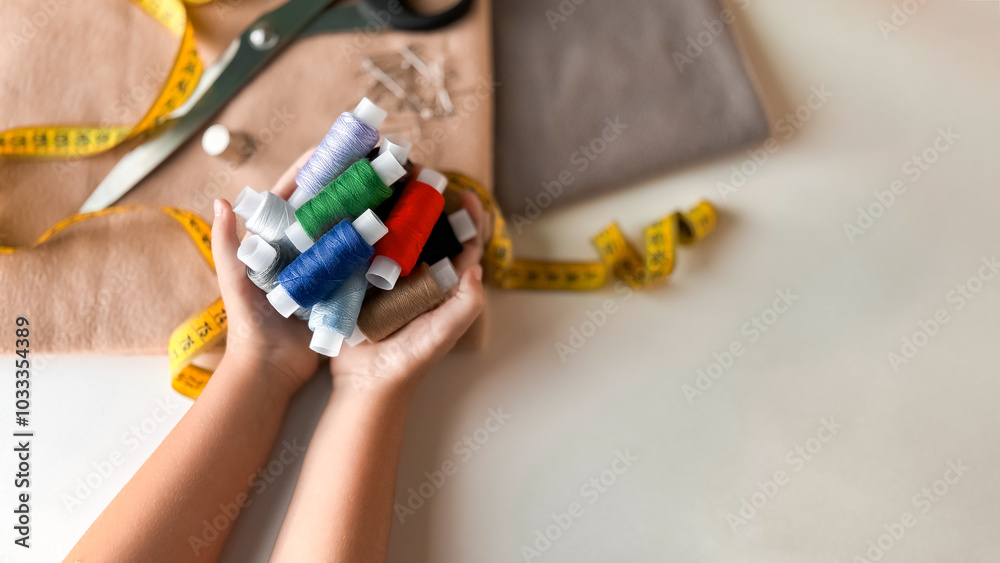 Colorful spools of thread in hands with sewing supplies on table Colorful spools of thread in hands with sewing supplies on table