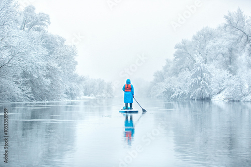 a man on a supboard in the winter on a river in the woods
