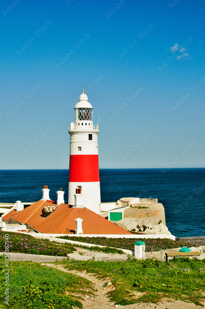 A lighthouse is on a rocky shoreline with a blue sky in the background A lighthouse is on a rocky shoreline with a blue sky in the background