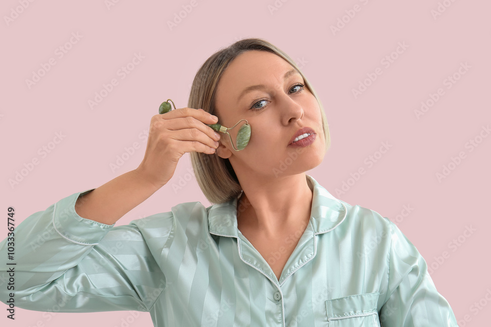 Woman using face massage roller on pink background Woman using face massage roller on pink background