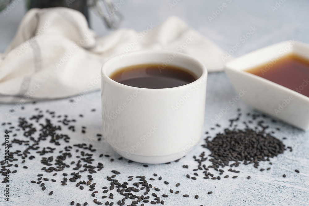 Obraz premium Cup of oil with sesame seeds on white grunge background