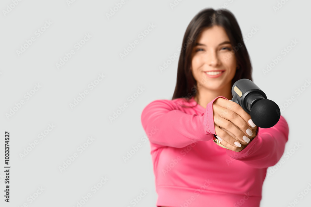 Sporty young woman with percussive massage gun on grey background Sporty young woman with percussive massage gun on grey background