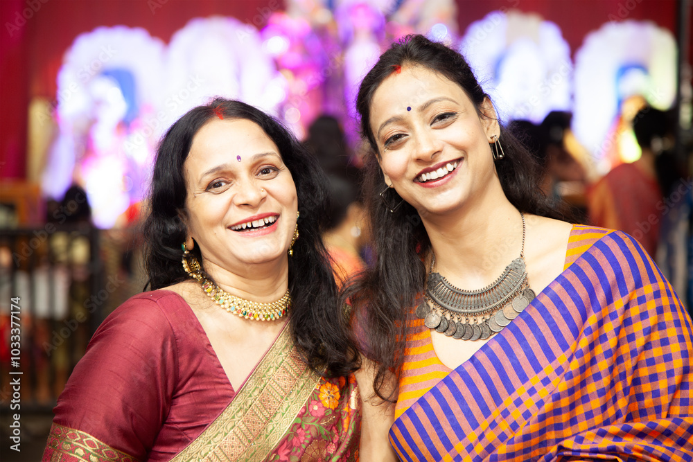Two joyful Indian women laughing and posing at a Durga Puja pandal during the Navratri festival, celebrating culture and togetherness. Two joyful Indian women laughing and posing at a Durga Puja pandal during the Navratri festival, celebrating culture and togetherness.