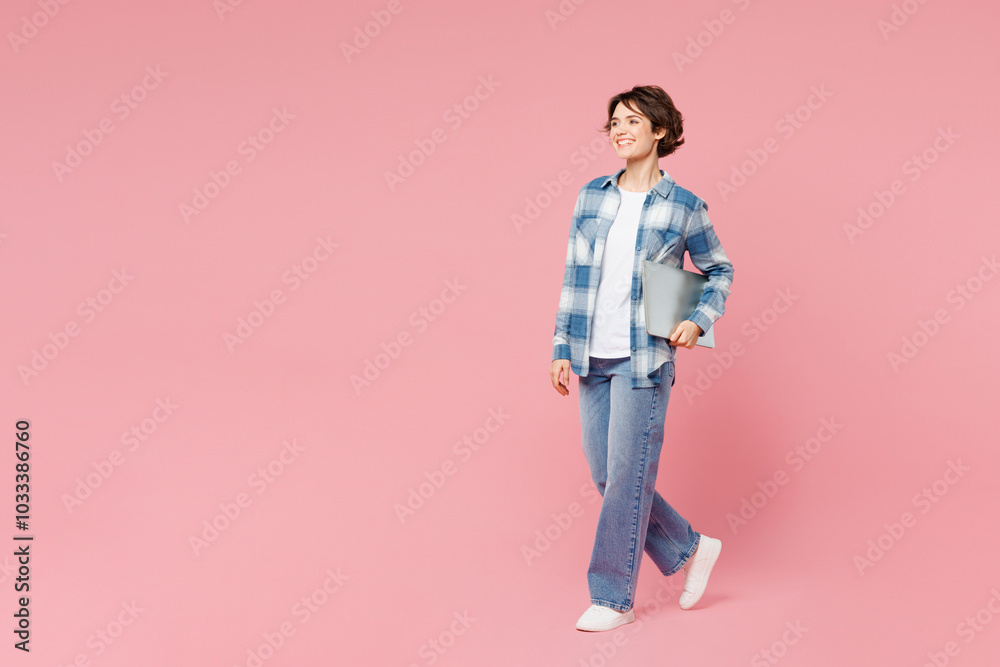 Full body side view young happy IT woman wear blue shirt white t-shirt casual clothes hold closed laptop pc computer isolated on plain pastel light pink background studio portrait. Lifestyle concept. Full body side view young happy IT woman wear blue shirt white t-shirt casual clothes hold closed laptop pc computer isolated on plain pastel light pink background studio portrait. Lifestyle concept.