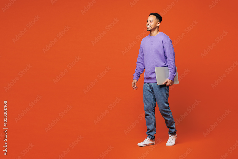 Full body young smart happy IT man of African American ethnicity wear purple sweatshirt casual clothes hold closed laptop pc computer isolated on plain red orange background studio. Lifestyle concept. Full body young smart happy IT man of African American ethnicity wear purple sweatshirt casual clothes hold closed laptop pc computer isolated on plain red orange background studio. Lifestyle concept.