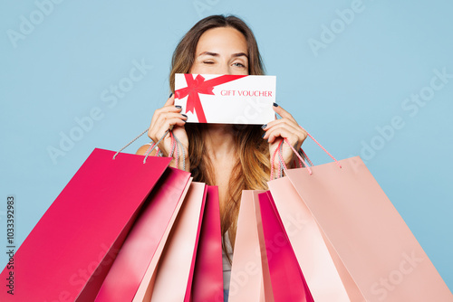 Close up young woman wear hold in hand paper package bags after shopping cover mouth with voucher card wink blink eye isolated on plain light pastel blue background. Black Friday sale buy day concept. photo