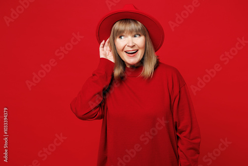 Elderly curious nosy blonde woman 50s years old she wearing sweater hat casual clothes try to hear you overhear listening intently isolated on plain red background studio portrait. Lifestyle concept.