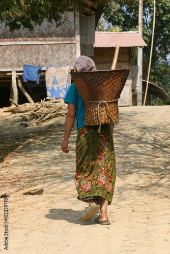 Bangladeshi rural tribal lady walking on a road with a traditional bucket on her back photo