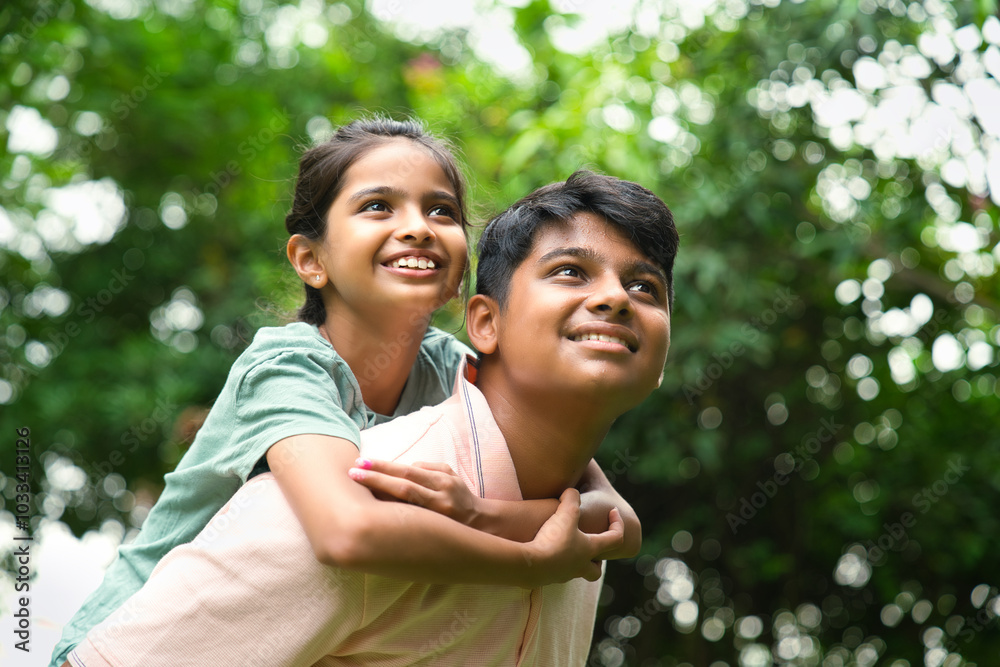 Indian big brother giving playful piggyback ride to his little sister outdoors in nature Indian big brother giving playful piggyback ride to his little sister outdoors in nature