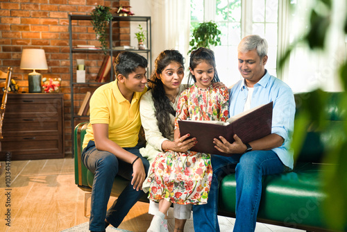 Canvas Print Indian family of four happily reminiscing while looking through a photo album in
