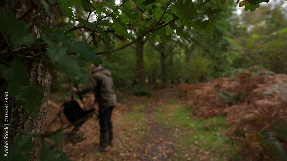 Shallow focus view of a man picking up his backpack and walking off through the woods