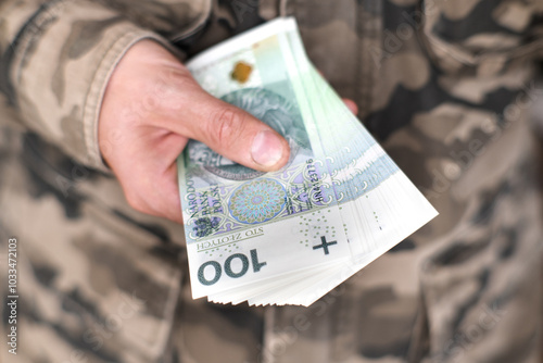 Army, military investments. A soldier holding Polish banknotes.
