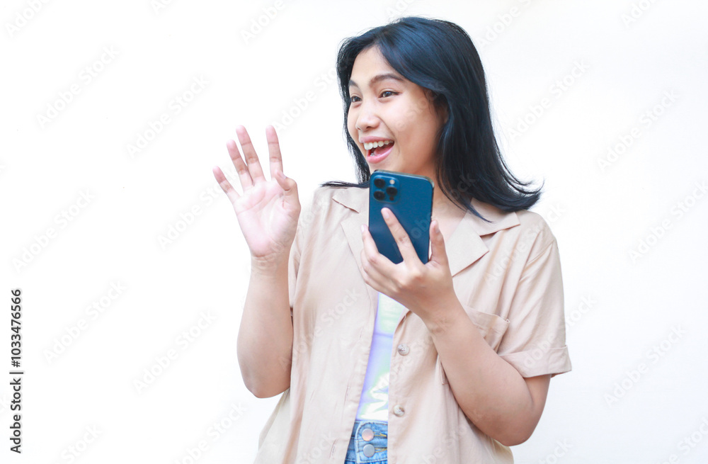 excited asian woman using smartphone and wave hand while talking in video call wearing casual brown clothes isolated on white background excited asian woman using smartphone and wave hand while talking in video call wearing casual brown clothes isolated on white background