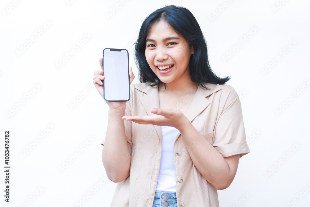 excited asian woman do presenting gesture with pointing finger to smartphone white screen wearing brown casual clothes isolated on white background excited asian woman do presenting gesture with pointing finger to smartphone white screen wearing brown casual clothes isolated on white background