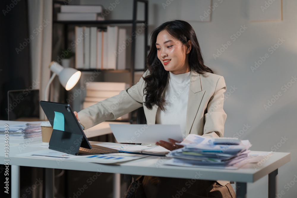 Focused and Determined: A young businesswoman diligently works on her laptop, surrounded by paperwork and a tablet. Focused and Determined: A young businesswoman diligently works on her laptop, surrounded by paperwork and a tablet.