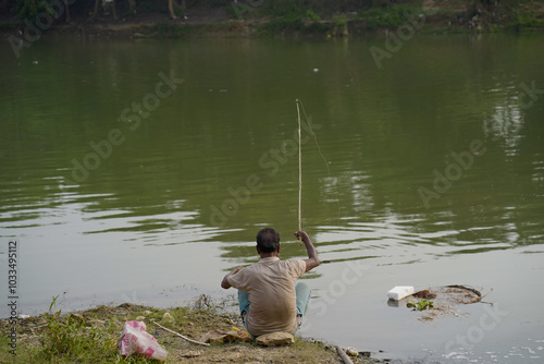 Desi Man Enjoying Fishing at the Riverbank, Desi Fisherman Sitting by Riverside, Man Enjoying Fishing at the Riverbank Stock Photo.  photo