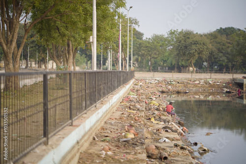 Boy Collecting Objects Amidst Immersion Ritual Debris, Polluted Pond After Visarjan Ritual with a Boy Searching, Aftermath of Durga Visarjan with Child Collecting Items, Boy Searching for Items,  photo