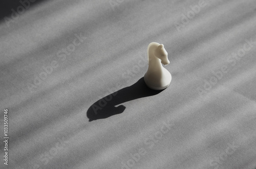 A white chess knight in bright sunlight casting a black shadow on a gray background, unconventional thinking, surprise and flexibility, freedom of thought, risk and adventurousness.