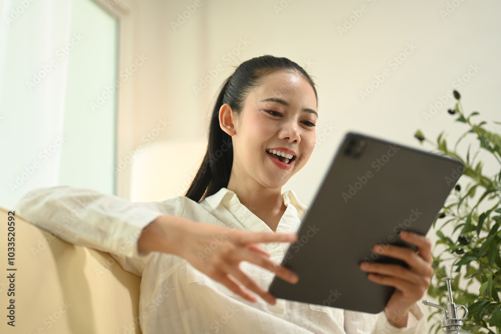Portrait of a happy young woman using digital tablet on sofa at home
