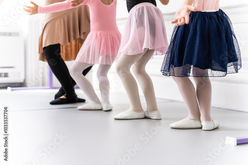 Little ballerinas standing in row behind their ballet teacher and practicing ballet