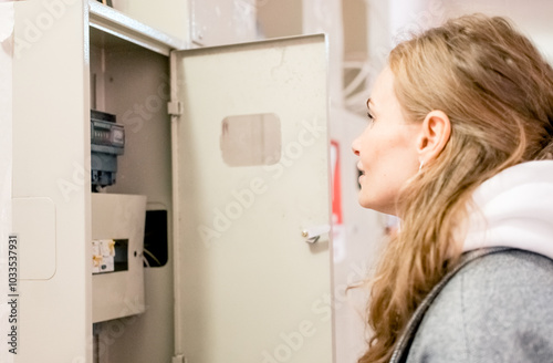 A young woman takes readings from an electric meter for further payment.