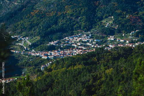 a picturesque village nestled in a lush, forested mountain landscape, with white and red-roofed houses scattered across the valley