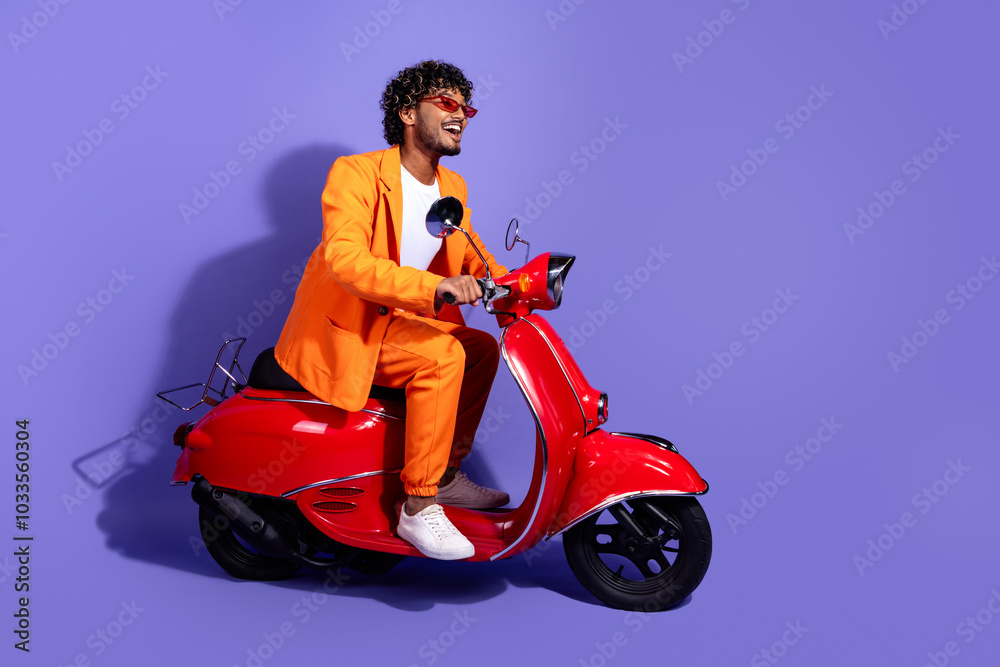 Full length photo of handsome good mood guy wear orange suit riding moped emtpy space isolated violet color background Full length photo of handsome good mood guy wear orange suit riding moped emtpy space isolated violet color background