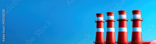 Four red and white industrial smokestacks stand against a clear blue sky, symbolizing energy production and environmental concerns.