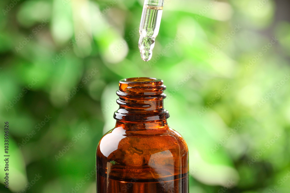 Essential oil dripping from pipette into bottle against blurred green background, closeup Essential oil dripping from pipette into bottle against blurred green background, closeup