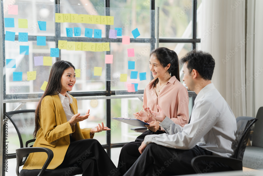 Brainstorming Session: Three colleagues gather around a large window covered in colorful sticky notes, engaging in a lively discussion about ideas and strategies for success.