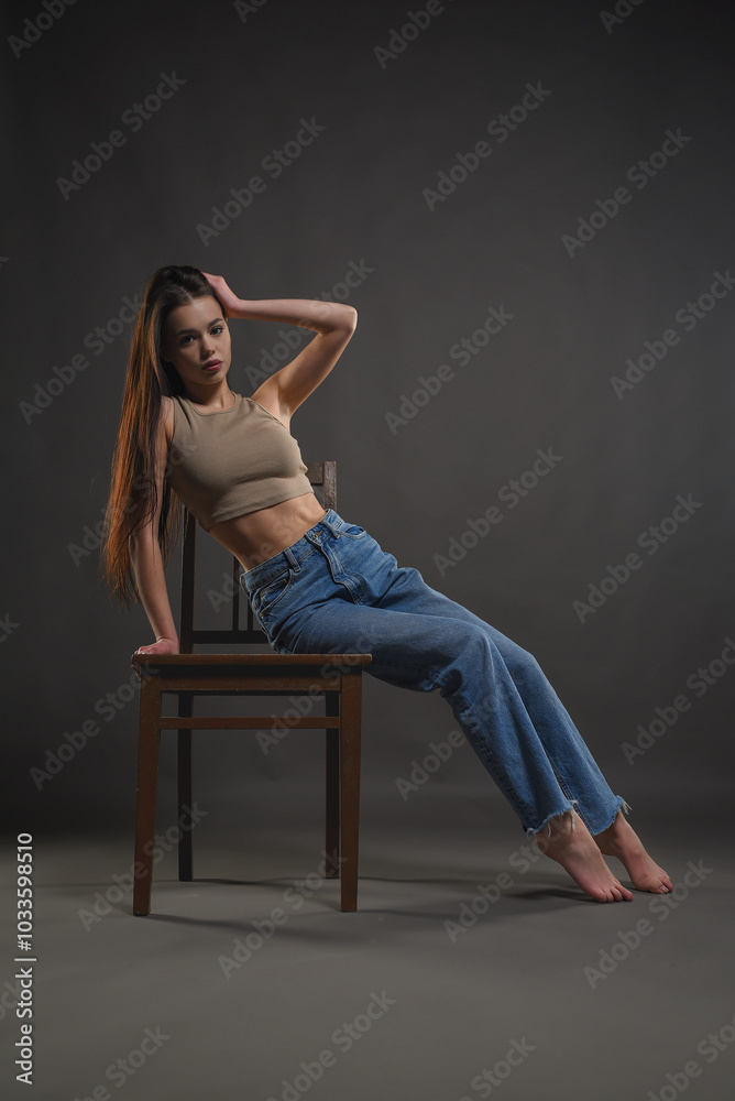 Beautiful girl posing with a chair on a gray background. Beauty and fashion. Beautiful girl posing with a chair on a gray background. Beauty and fashion.