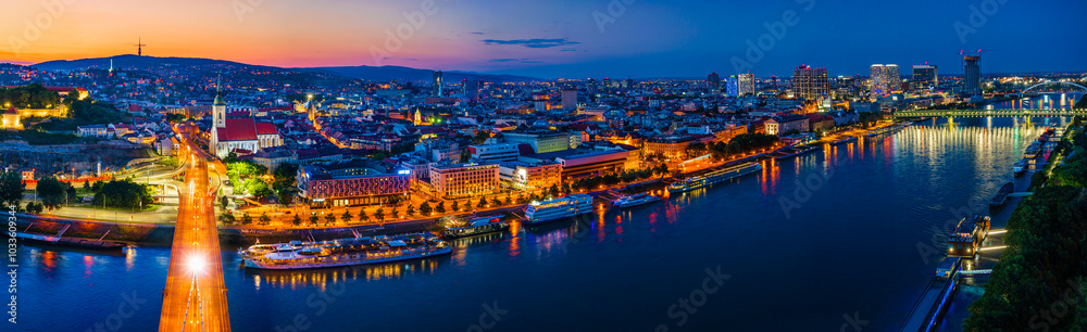 Naklejka premium Bratislava, Slovakia - June 2022: City skyline on the shores of the Danube river; Bratislava castle, the old town, Eurovea; UFO bridge; SNP bridge; Appolo Bridge