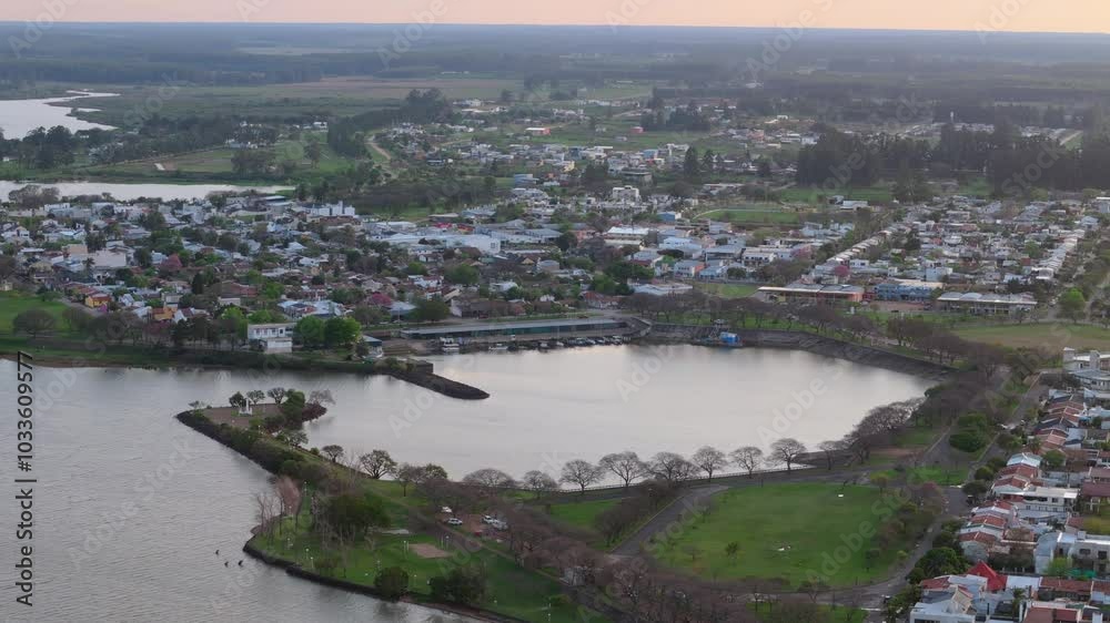 Aerial shot of a town beside a waterbody at sunset, showcasing houses, roads, and greenery, with a serene and picturesque atmosphere in Federacion, Entre Ríos, Argentina Aerial shot of a town beside a waterbody at sunset, showcasing houses, roads, and greenery, with a serene and picturesque atmosphere in Federacion, Entre Ríos, Argentina