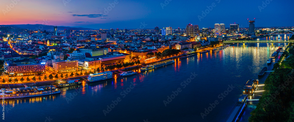 Fototapeta premium Bratislava, Slovakia - June 2022: City skyline on the shores of the Danube river; Bratislava castle, the old town, Eurovea; UFO bridge; SNP bridge; Appolo Bridge