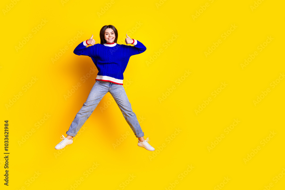 Full length photo of pretty teen girl jumping thumb up wear trendy knitwear blue outfit isolated on yellow color background Full length photo of pretty teen girl jumping thumb up wear trendy knitwear blue outfit isolated on yellow color background