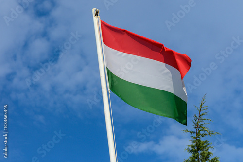 Hungarian flag waving proudly against a clear blue sky with a few clouds visible in the background during a bright sunny day