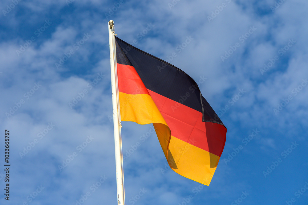 German flag waving proudly against a blue sky with scattered clouds during a sunny day German flag waving proudly against a blue sky with scattered clouds during a sunny day