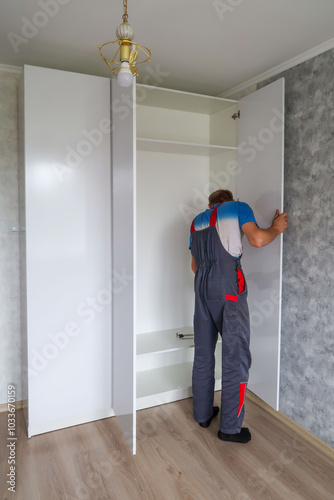 A man in a blue and red jumpsuit is opening a closet door