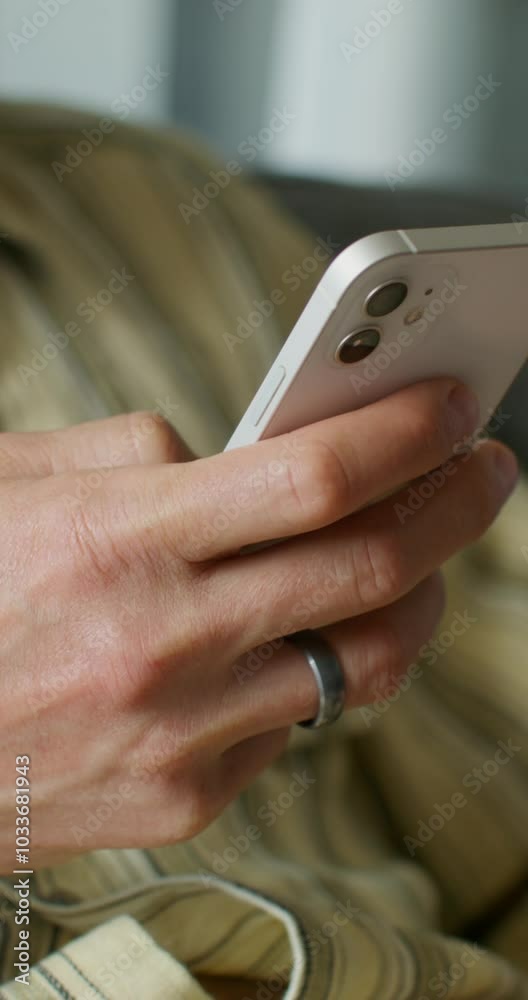 A man is typing on a mobile phone sitting on the couch at home. close-up of his hands, an unrecognizable person. Daylight A man is typing on a mobile phone sitting on the couch at home. close-up of his hands, an unrecognizable person. Daylight
