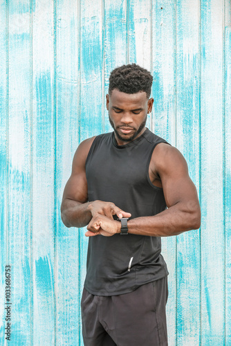 Athletic man checking smartwatch during outdoor workout in urban setting with light blue wooden background