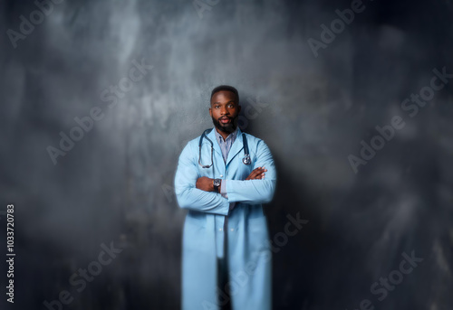 A man wearing a blue lab coat stands against a gray background with his arms crossed.