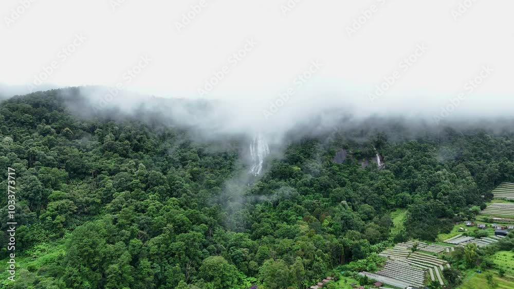 Aerial view of beautiful waterfall village in the lush green rain cloud and foggy cover tropical rain forest mountain during the rainy season. Beautiful landscape with high mountain Aerial view of beautiful waterfall village in the lush green rain cloud and foggy cover tropical rain forest mountain during the rainy season. Beautiful landscape with high mountain