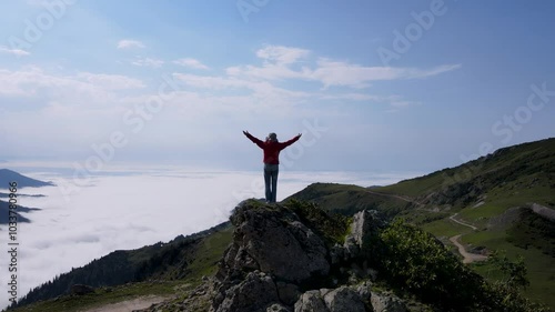 Footage of a woman watching nature with her arms open at the top of the mountain.
