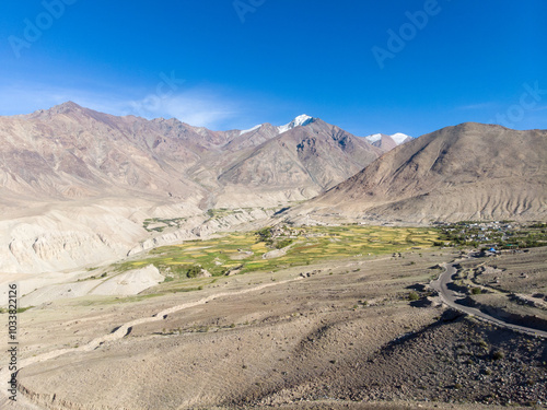 A serene valley with patches of greenery surrounded by rugged mountains under a clear sky.