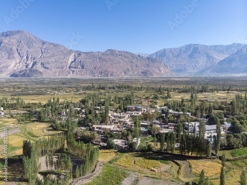 Fotografie Aerial view of a lush green valley with a village surrounded by arid mountains