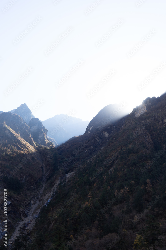 A serene mountain range under the clear sky with sunlight peeking over the peaks. A serene mountain range under the clear sky with sunlight peeking over the peaks.
